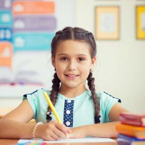 Smiling Girl Writing With Textbooks Beside Her